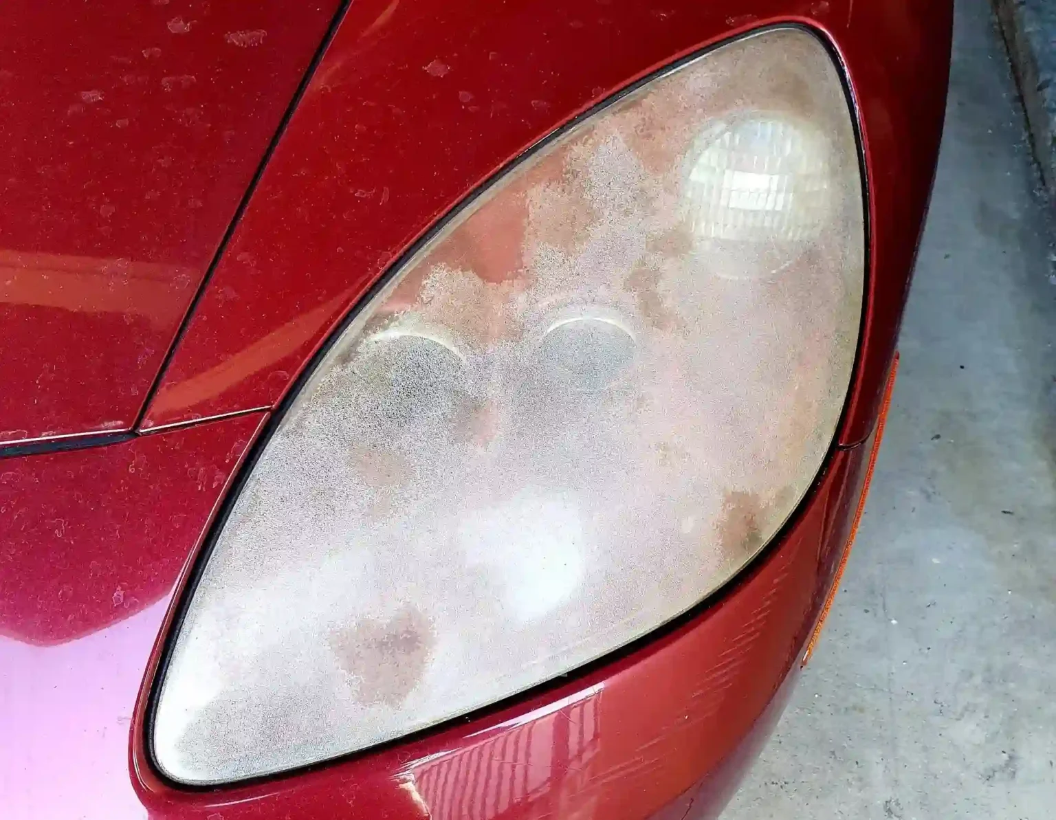 Scaled and Oxidized Headlights of a Red Car